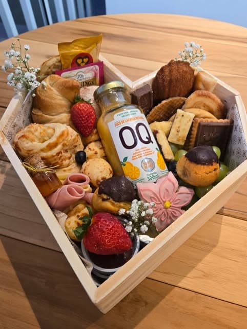 Cesta da Platteria em caixa de madeira em formato de coração, com frutas, pães, doces e flores.